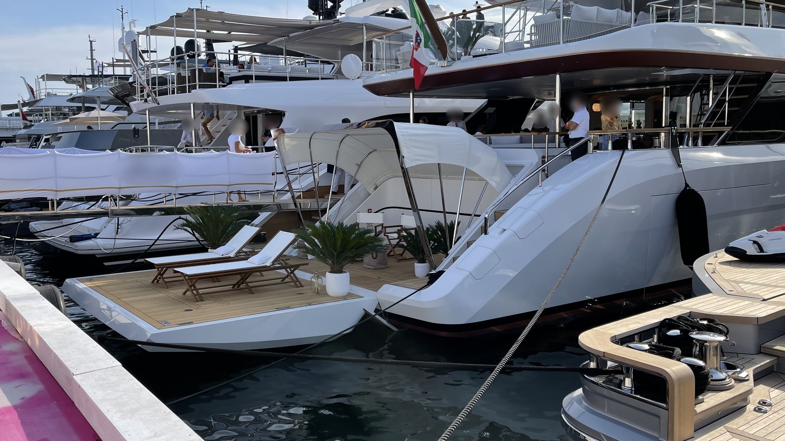 Motor yachts with sun loungers on their swim platforms moored at a boat show pontoon