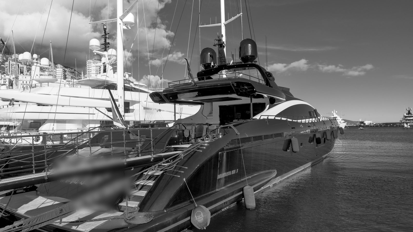 Black and white photo of superyachts and sailing yachts moored stern-to along a quay in a Mediterranean marina