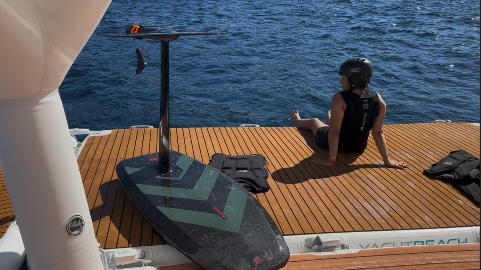 An eFoil, life vests and a rider in helmet and impact vest on the teak swim platform of a superyacht at sea