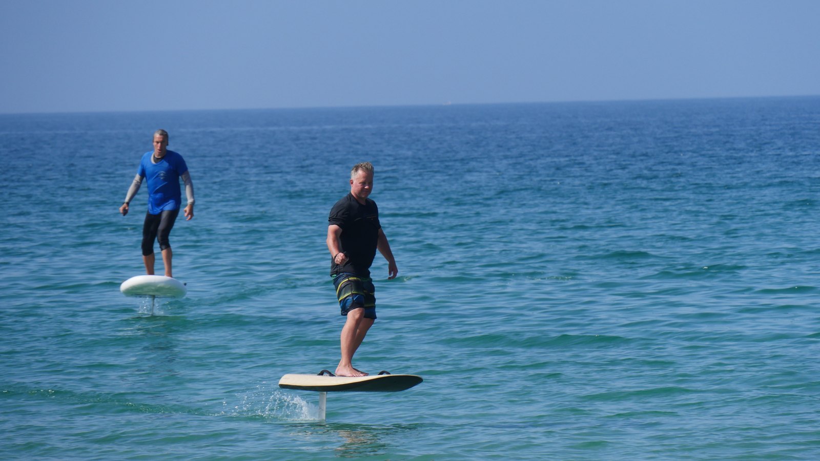 Two riders flying on eFoils above clear blue sea, one in front and one behind
