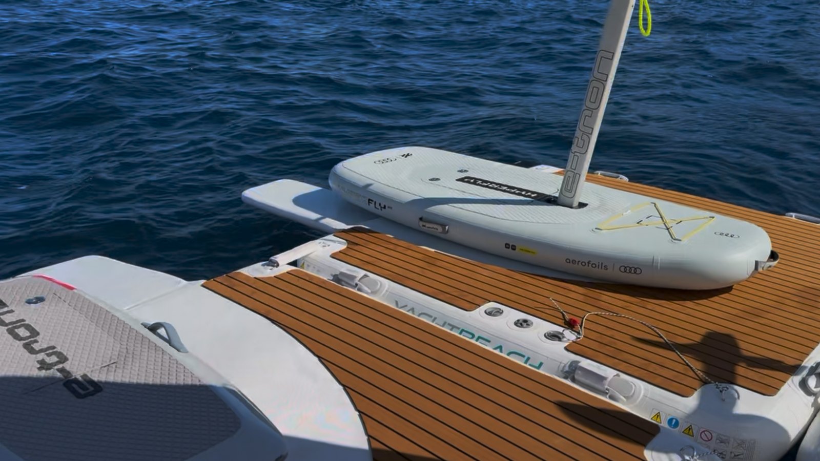 An eFoil scooter lying on the teak-look deck of an inflatable swim platform tied behind a yacht at sea