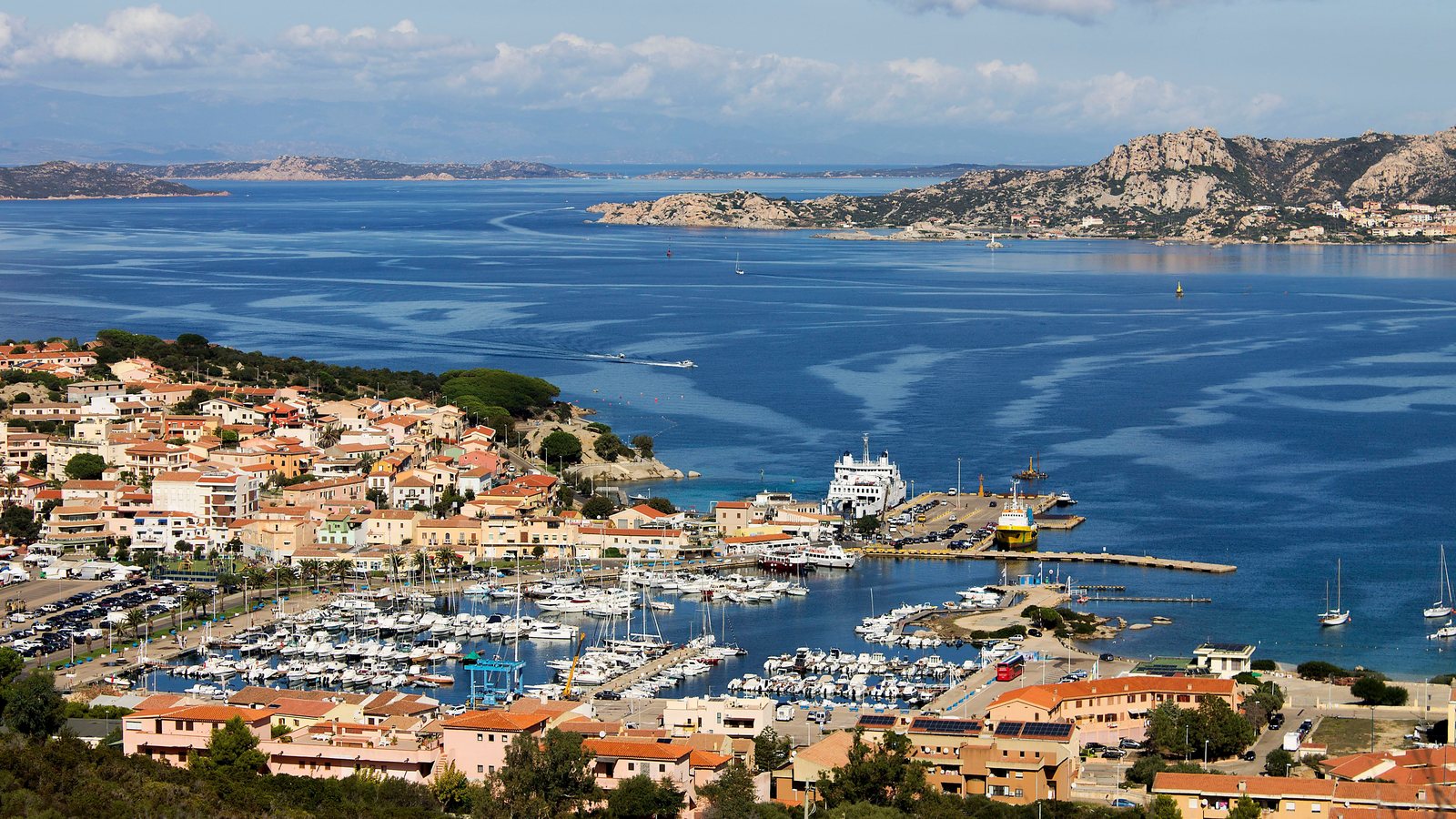Harbour full of boats below a hillside town in northern Sardinia, islands in the bay behind