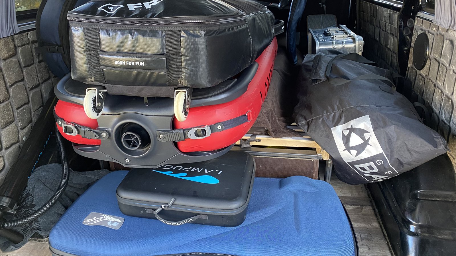 A red jetboard with a board bag on top, a battery case and padded board bags packed together in the back of a van