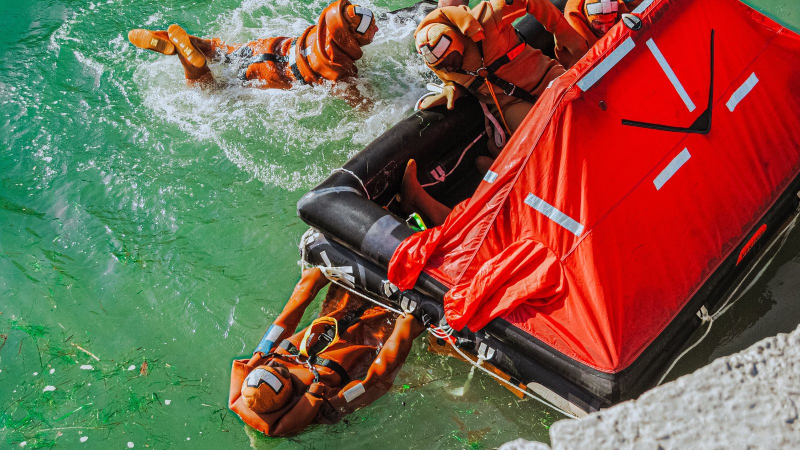 Crew in orange survival suits climbing into a red canopied life raft during sea survival training