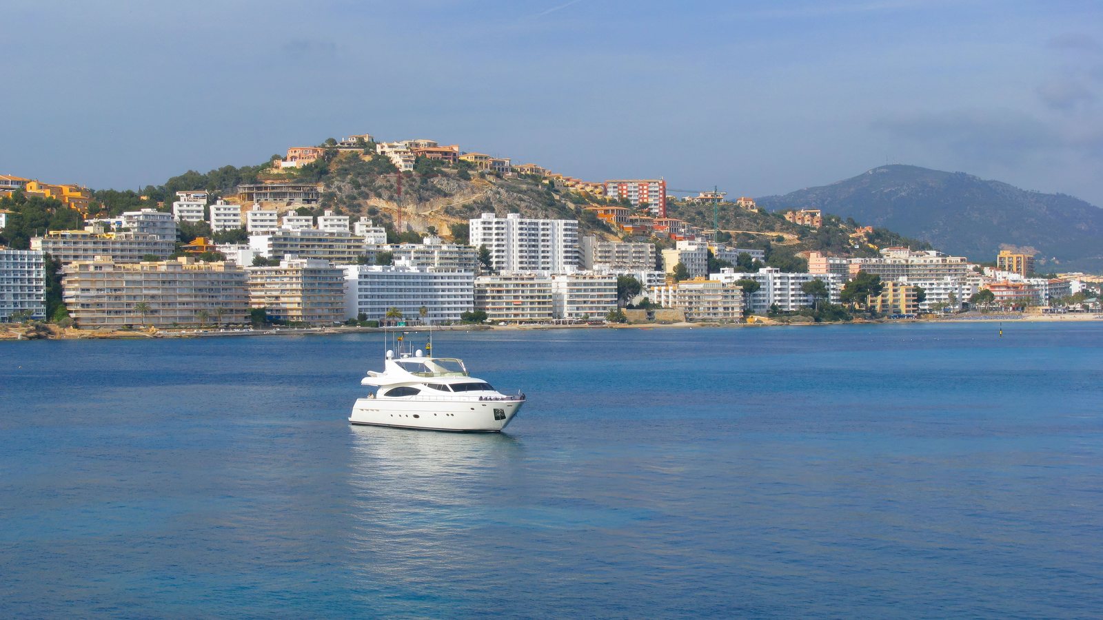 Motor yacht at anchor in a bay off the coast of Mallorca, hotels and hills behind