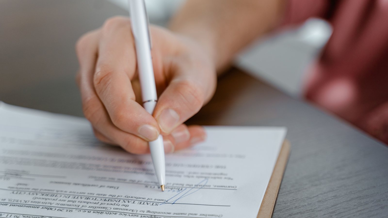 Close-up of a hand signing a document with a white pen