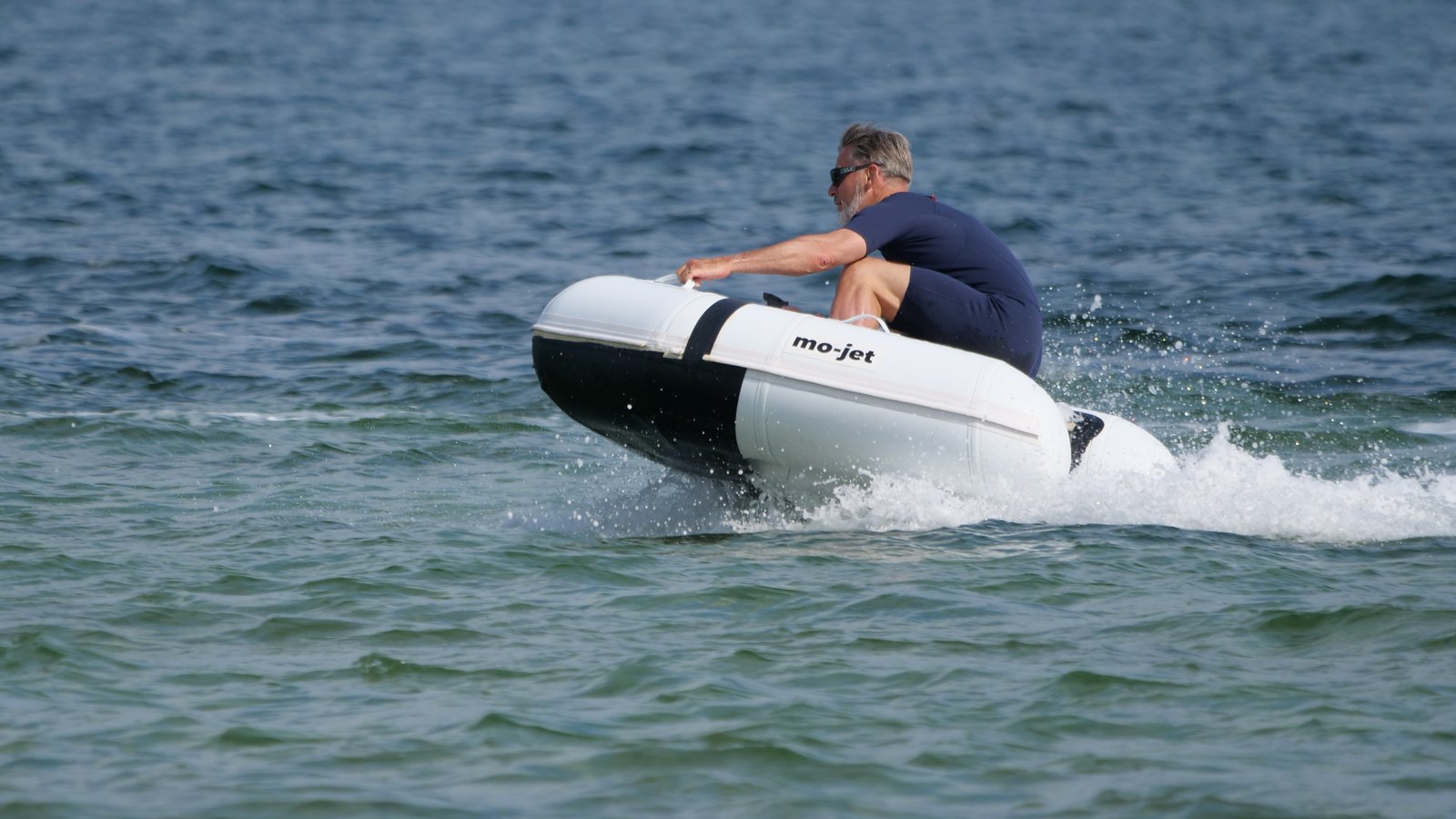 A small white electric tender with a jet drive banking through a turn at speed on choppy water