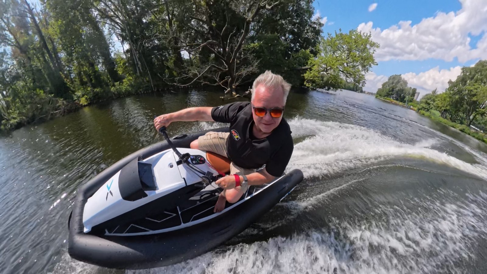 A rider in sunglasses leaning into a tight turn on a white and black electric jet ski on a tree-lined river