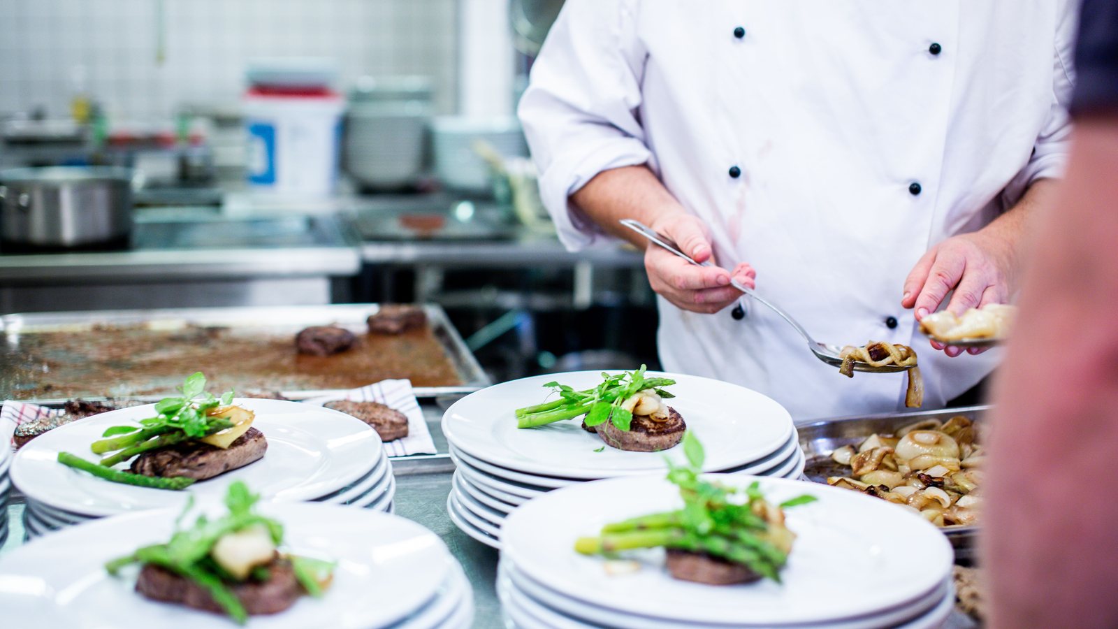 Chef in a white jacket plating several dishes in a professional kitchen