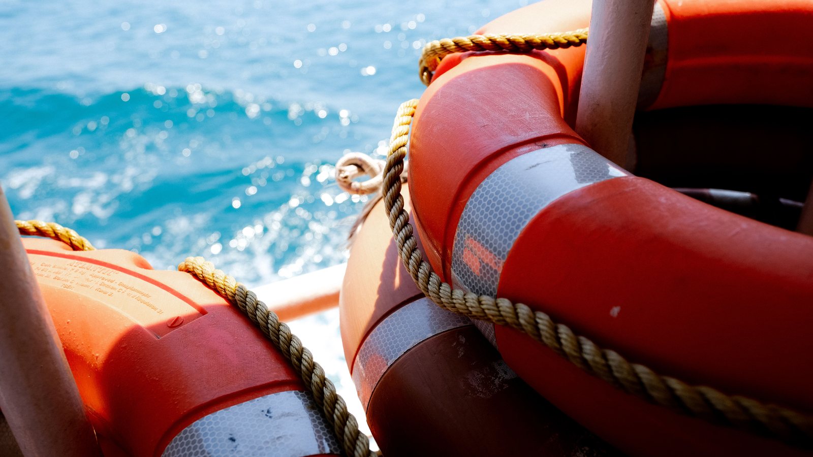 Orange lifebuoys with reflective tape and rope on the rail of a vessel, sea in the background