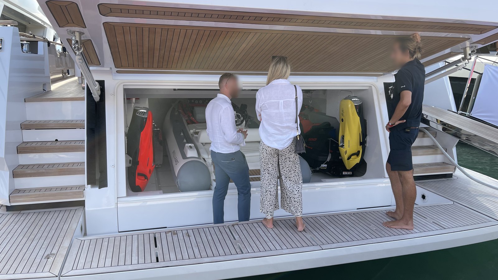 Three people at the open tender garage of a superyacht holding a tender, a jet ski and two underwater scooters