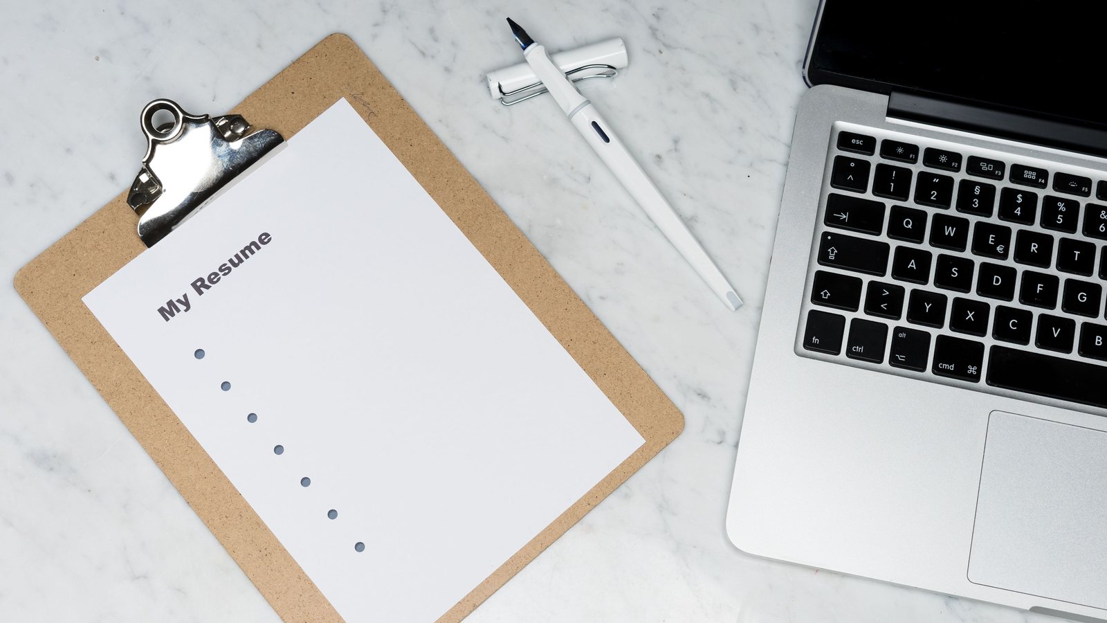 Clipboard with a sheet headed My Resume next to a fountain pen and a laptop on a marble desk